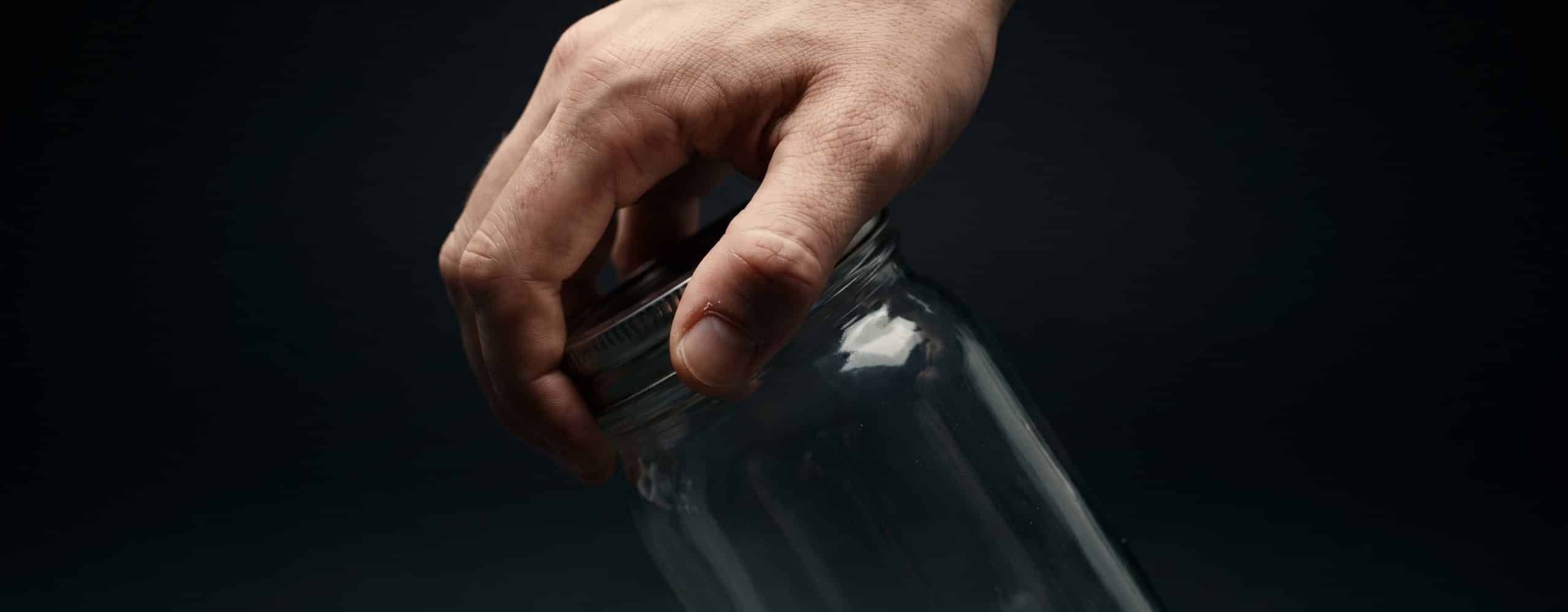 Main saisissant le couvercle d'un bocal en pince pouce-index, tension visible à la base du pouce